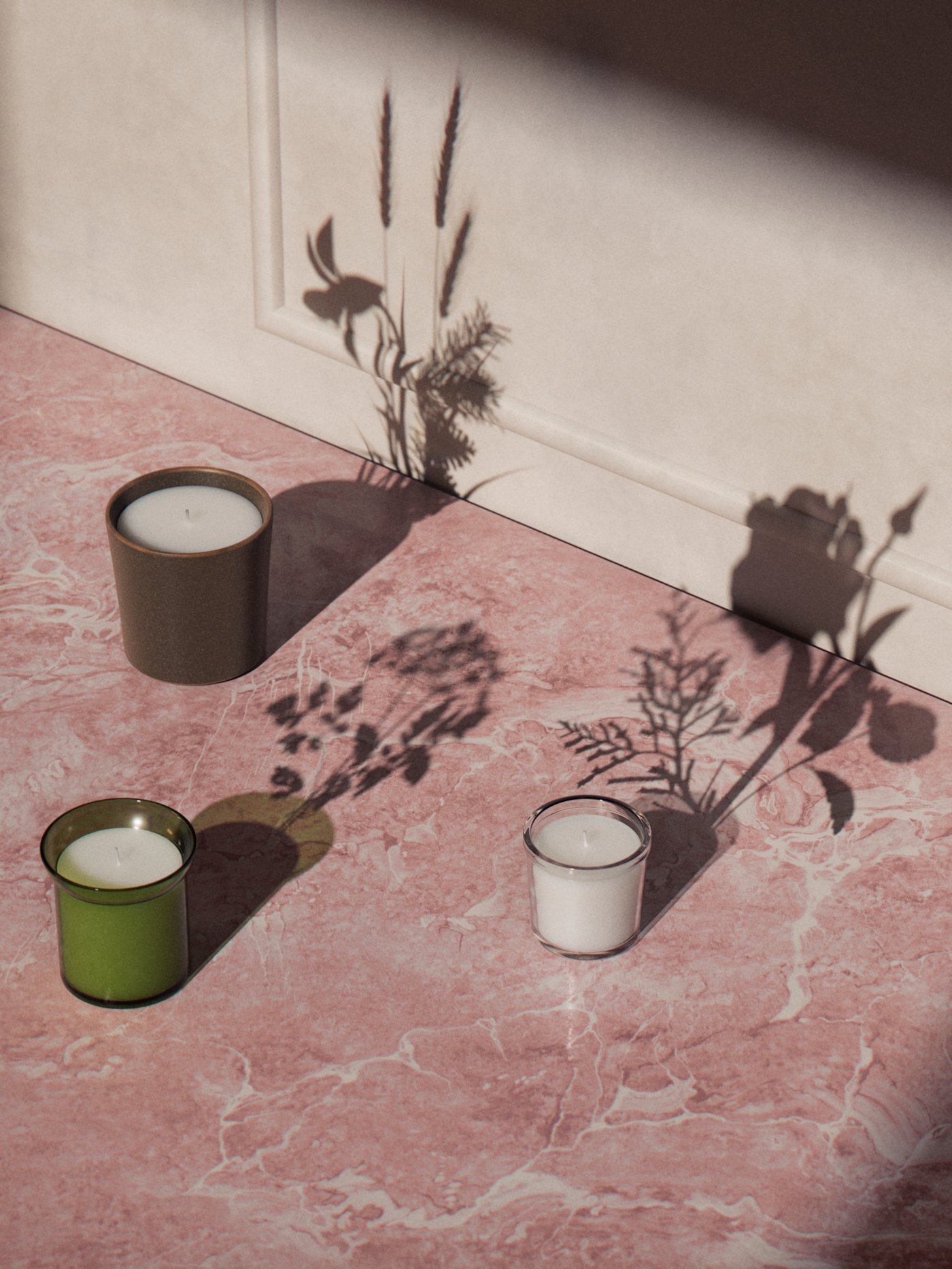 Tres velas aromáticas HEDERSAM, ADLAD y ENSTAKA sobre una cubierta de mármol rosa.