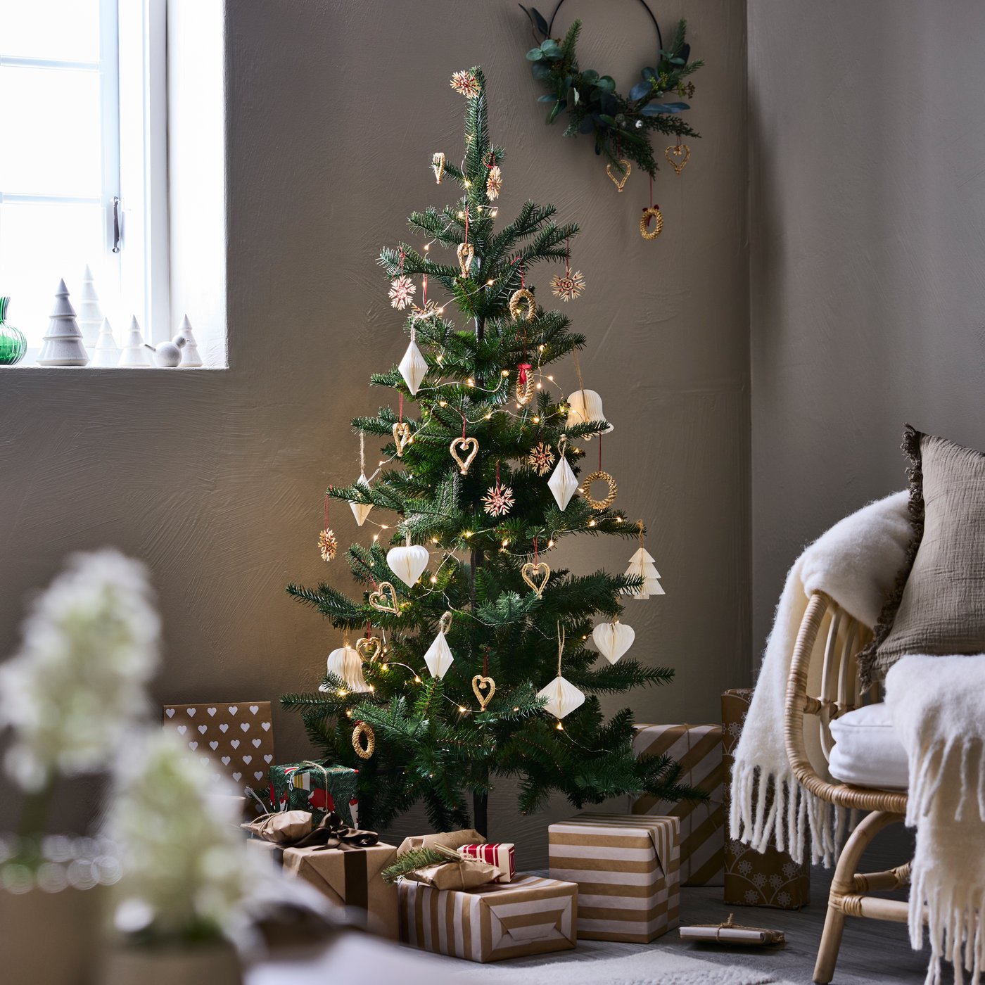 Una sala en tonos beige con un árbol navideño en el centro. Al costado del árbol un sillón.