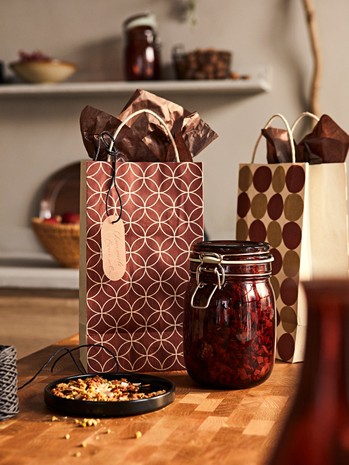 Two KRÖSAMOS gift bags with labels and wrapping paper and a KRÖSAMOS glass jar with lid filled with a herbal tea blend.