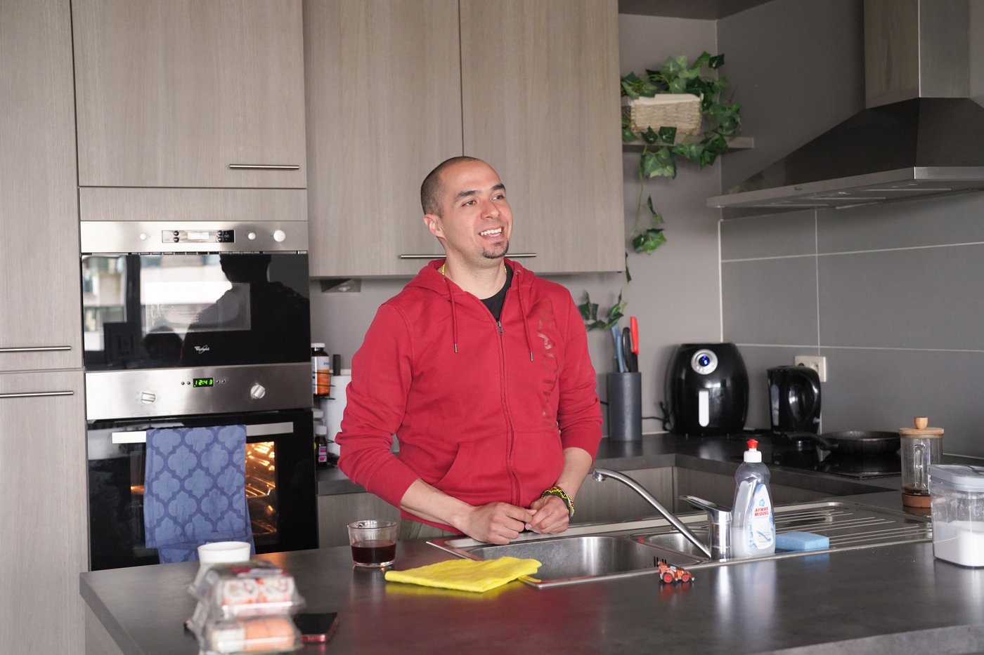 Edgar, wearing a red hoodie, stands in his kitchen.