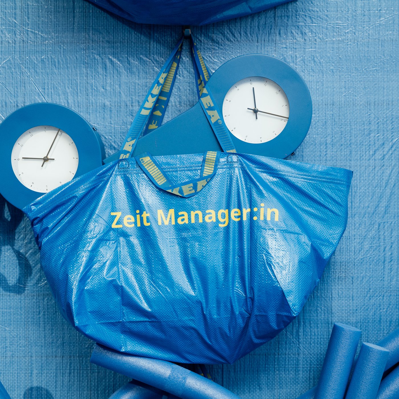 Eine FRAKTA Tasche mit der Aufschrift "Zeit Manager:in" gefüllt mit zwei IKEA PS Uhren in blau.