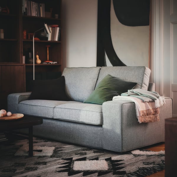 A grey KIVIK 2‑seater sofa with a green SANELA cushion on a TANNISBY rug in the living room.