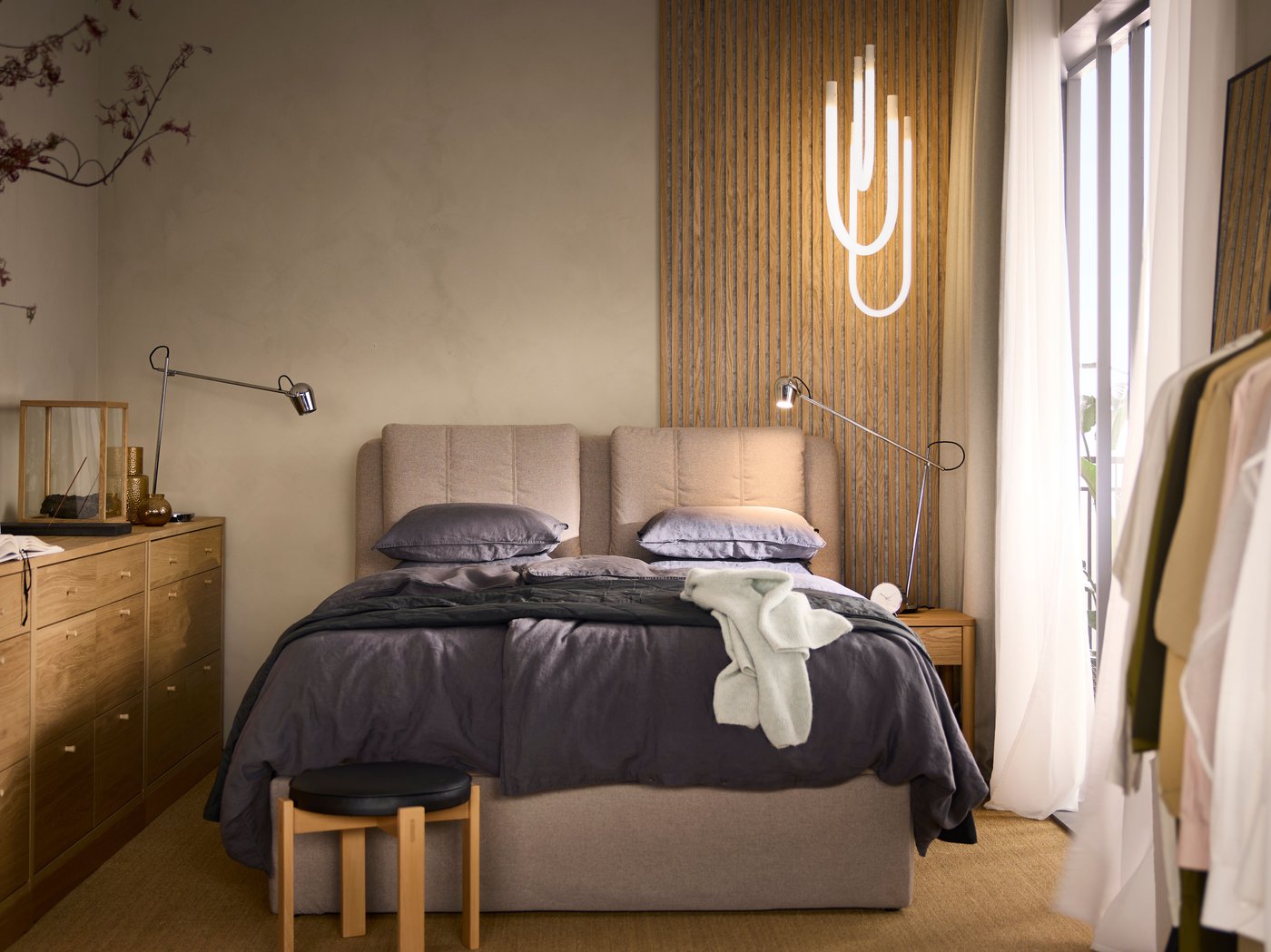 A LILLFJÄLLET divan bed with storage with dark grey bed linen by a beige wall with a VARMBLIXT LED light hanging above it.
