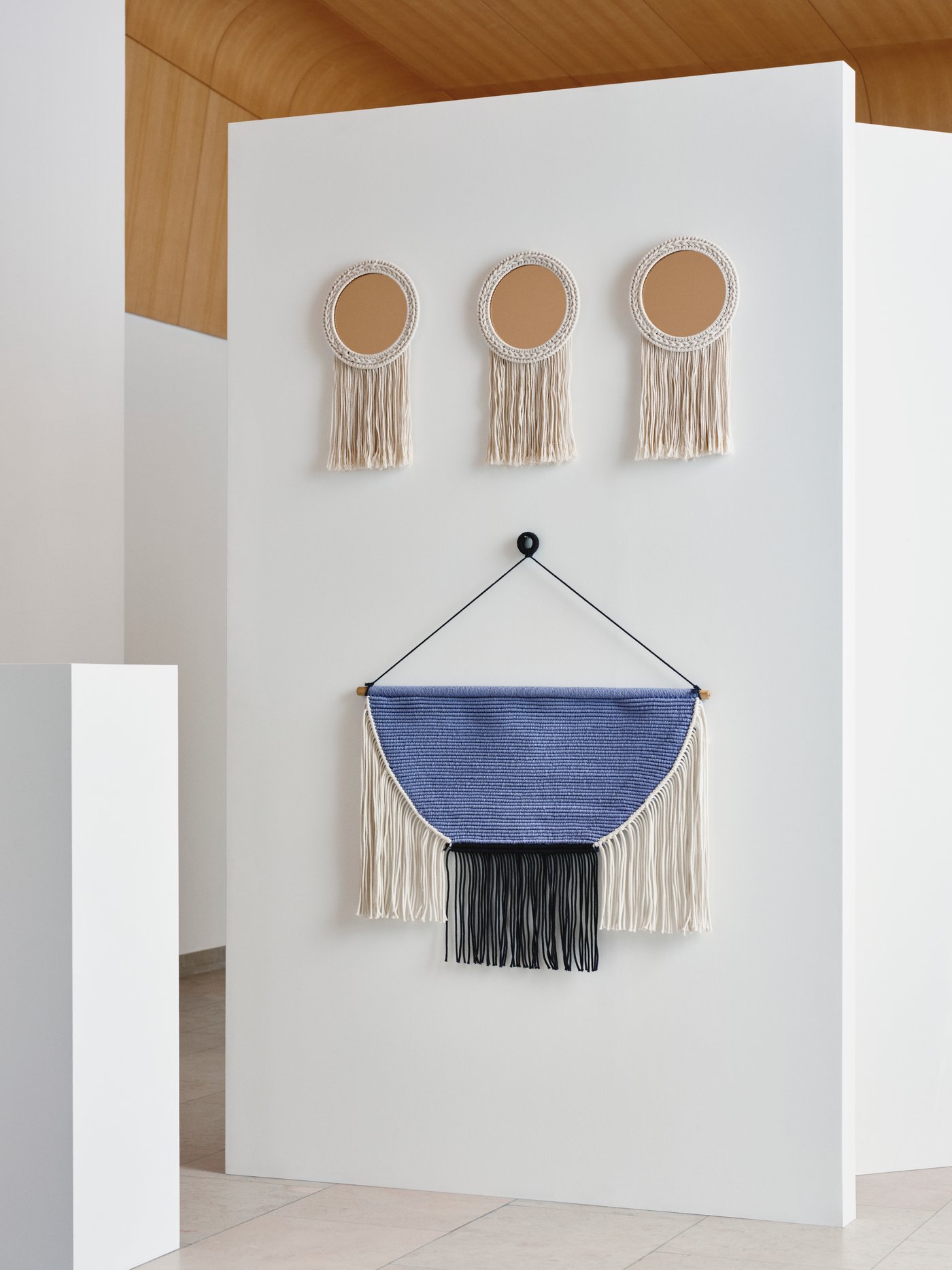 A HÄNGALM hanging tapestry in beige black/light lilac-blue hangs from a white wall, underneath three ENERGISKOG mirrors.