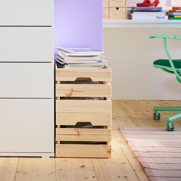 Une pièce avec une commode à quatre tiroirs VIHALS blanche, avec un mur violet et un plancher en bois, à côté de boîtes en bois naturel.