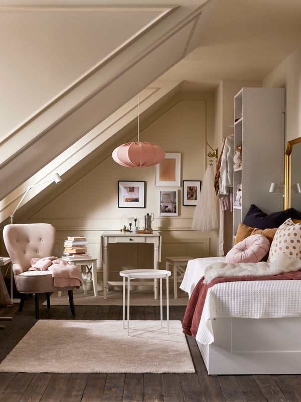 Una recámara luminosa con un diván-cama, una alfombra beige, una charola blanca GLADOM, un estante blanco, un sillón beige y una lámpara de techo rosa.