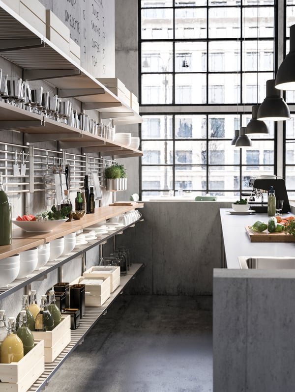 KUNGSFORS suspension shelf behind a café counter with a coffee machine. Open shelves hold coffee pots, bowls, and food.
