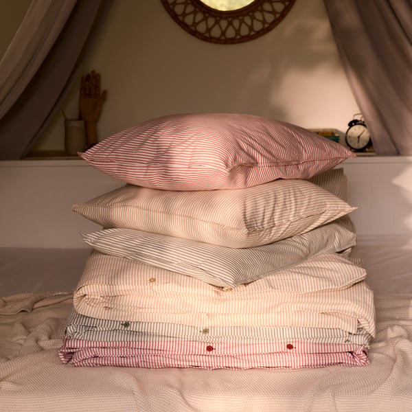 A pile of striped SOLFIBBLA duvet covers and pillows in red, blue and yellow, on top of HEMNES day-bed.