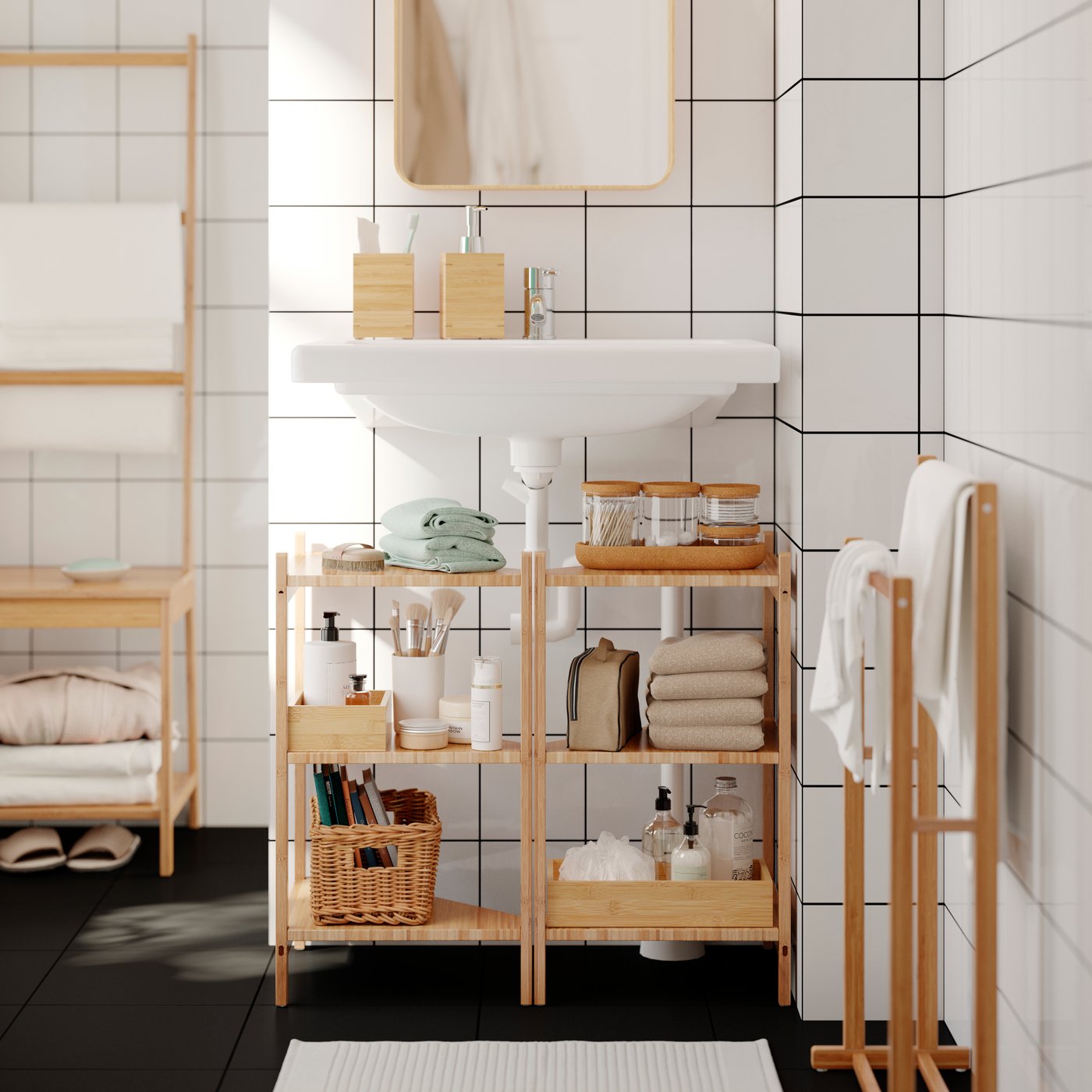 In einem Badezimmer sind zwei RÅGRUND Waschbecken-/Eckregale aus Bambus mit Toilettenartikeln gefüllt unter einem Waschbecken zu sehen.  An einer Handtuchstange hängen Handtücher.