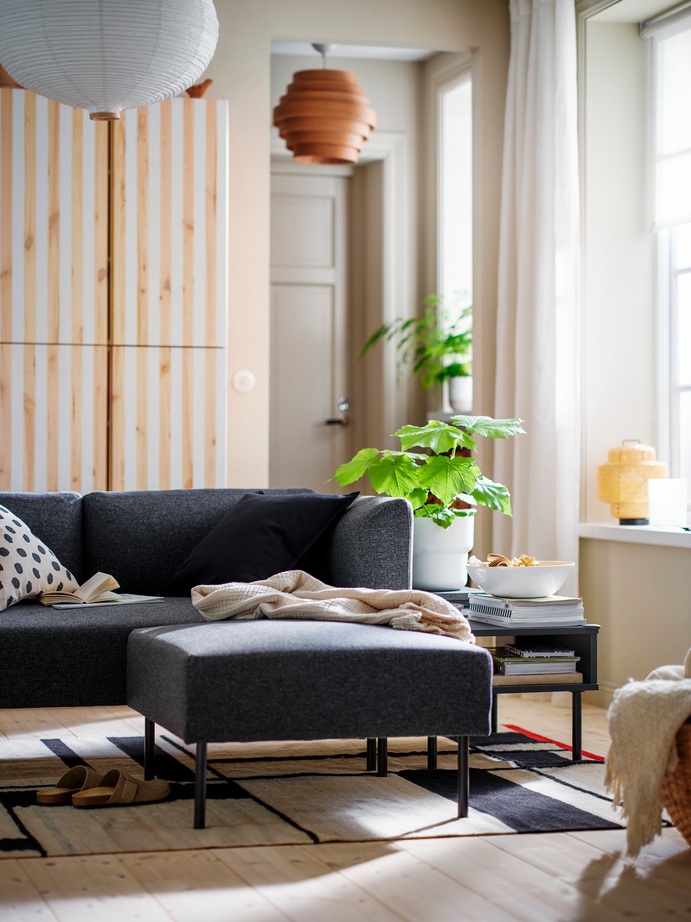 A TUNSTA side table with a plant in a pot on top stands on a RASTPLATS rug at the side of some modular LILLEHEM seating