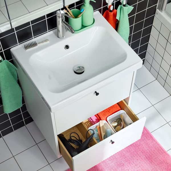 Ein Badezimmer mit weiß/schwarzen Fließen, einem Waschbecken mit Unterschrank und bunten Badaccessoires.