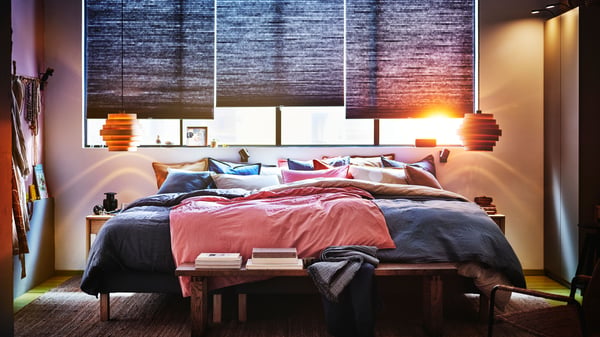 A bedroom with three blue HOPPVALS roller blinds on the window for an extra layer of insulation in the winter.