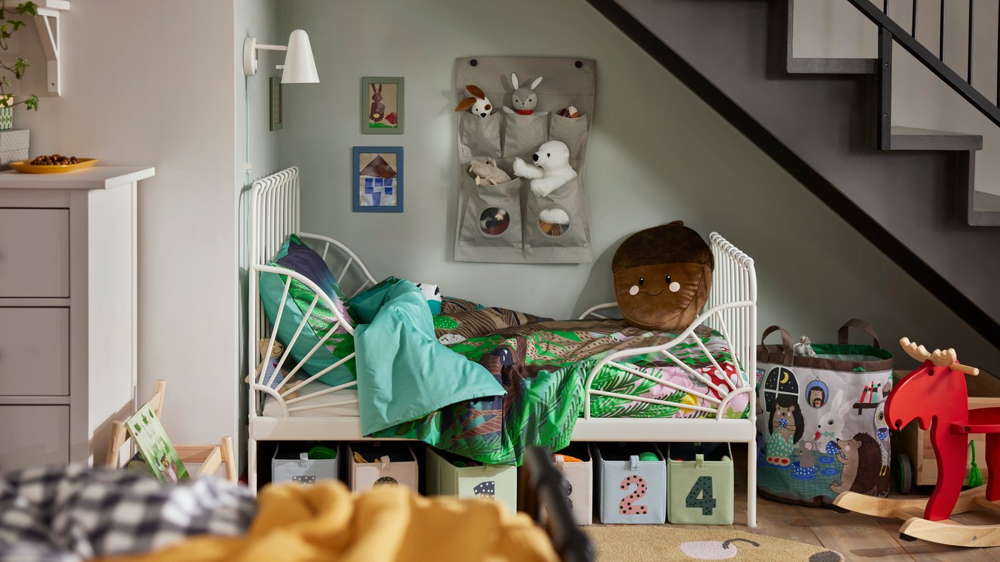 MINNEN extendable children’s bed in a corner of the room, with numbered storage boxes below and soft toys above.