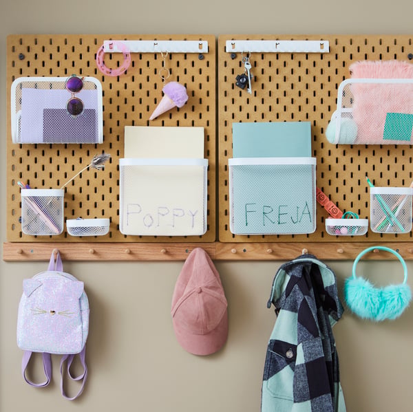 Children’s school accessories arranged on side-by-side SKÅDIS wood pegboards, above garments hung on HÖVOLM six-knob racks.