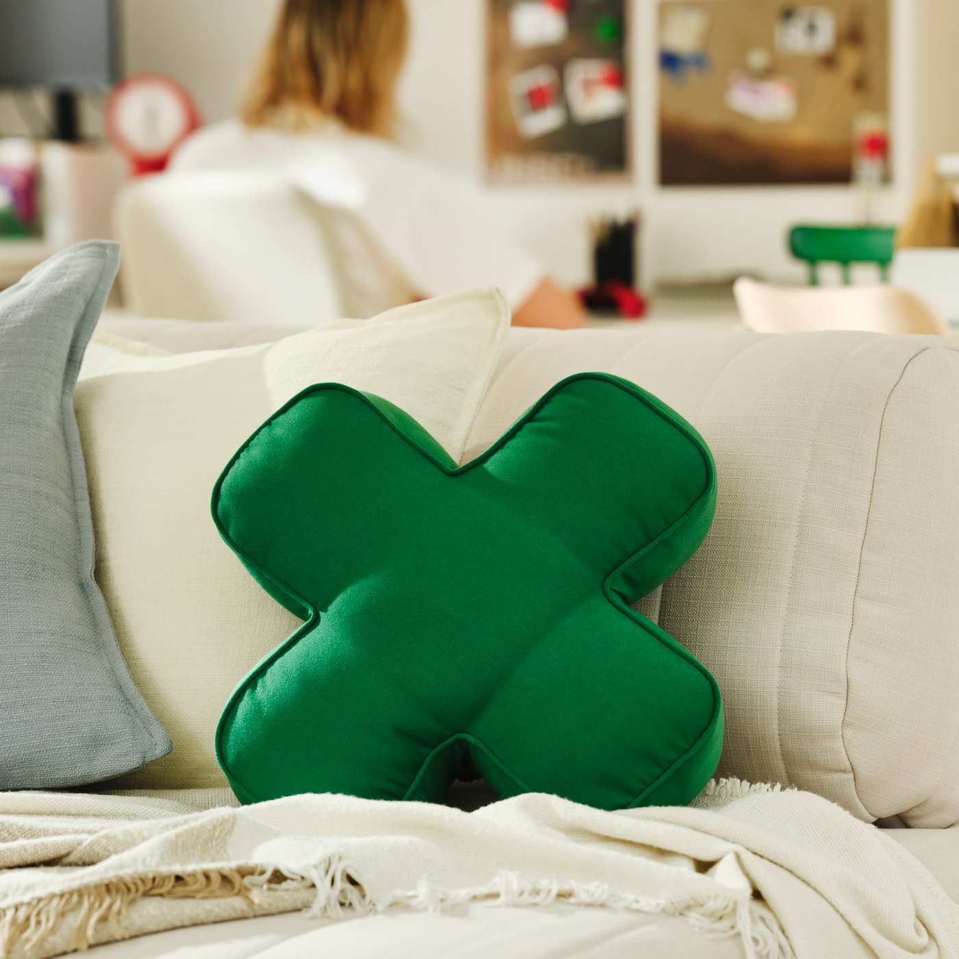Close-up of an YXSTABY gaming D-pad cushion on a white sofa with a person sitting at a desk in the background.