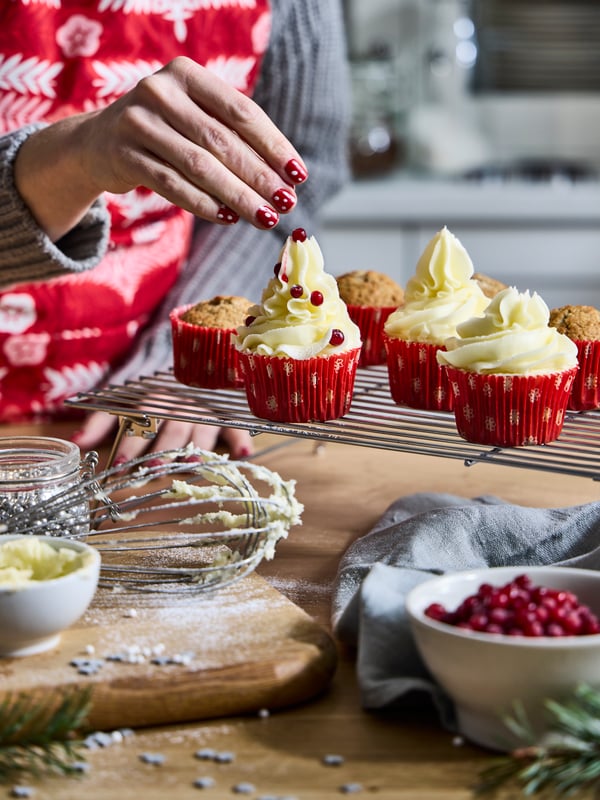 Someone is baking cupcakes in VINTERFINT red moulds with an acacia SMÅÄTA chopping board in the kitchen.