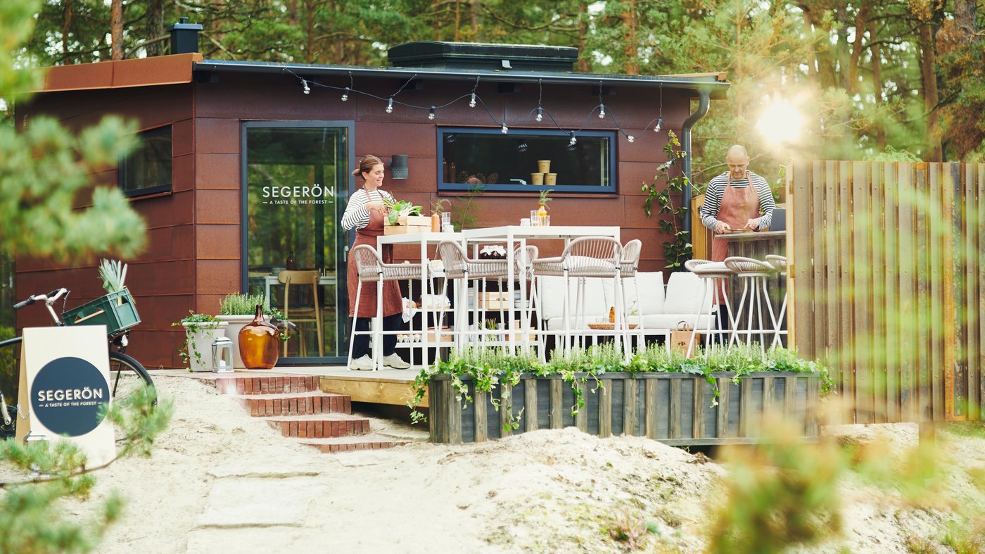 Zwei Personen richten ein Pop-up-Restaurant im Wald ein. Dazu stellen sie auf der Terrasse SEGERÖN Möbel für draußen auf.