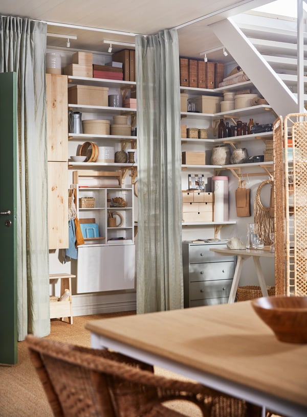 A corner of a room with VIDGA track set and SILVERLÖNN sheer curtains pulled open to show a busy work and storage area.