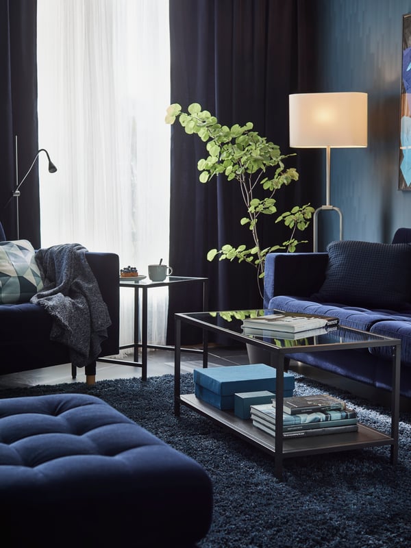 A blue LANDSKRONA sofa, footstool and armchair with one glass coffee table between them and another beside the armchair.