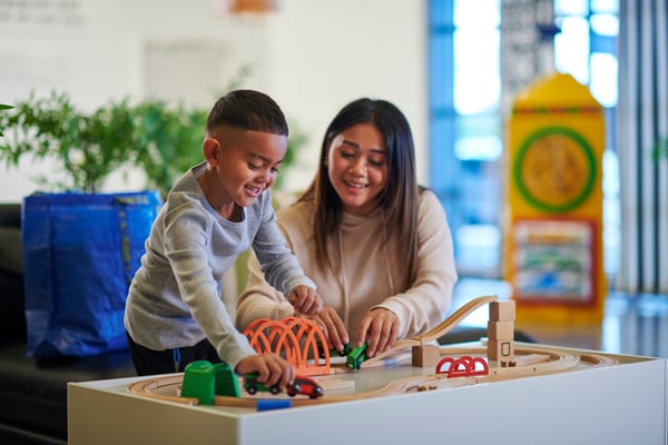Eine Mutter spielt mit ihrem Sohn mit einer Spielzeugeisenbahn im Spielbereich im IKEA Einrichtungshaus
