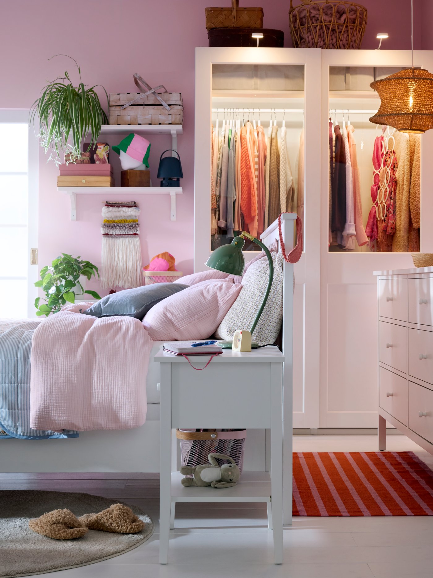 Bedroom with white bed, bedside table and chest of drawers, pink walls and a PAX/GRIMO wardrobe in back.
