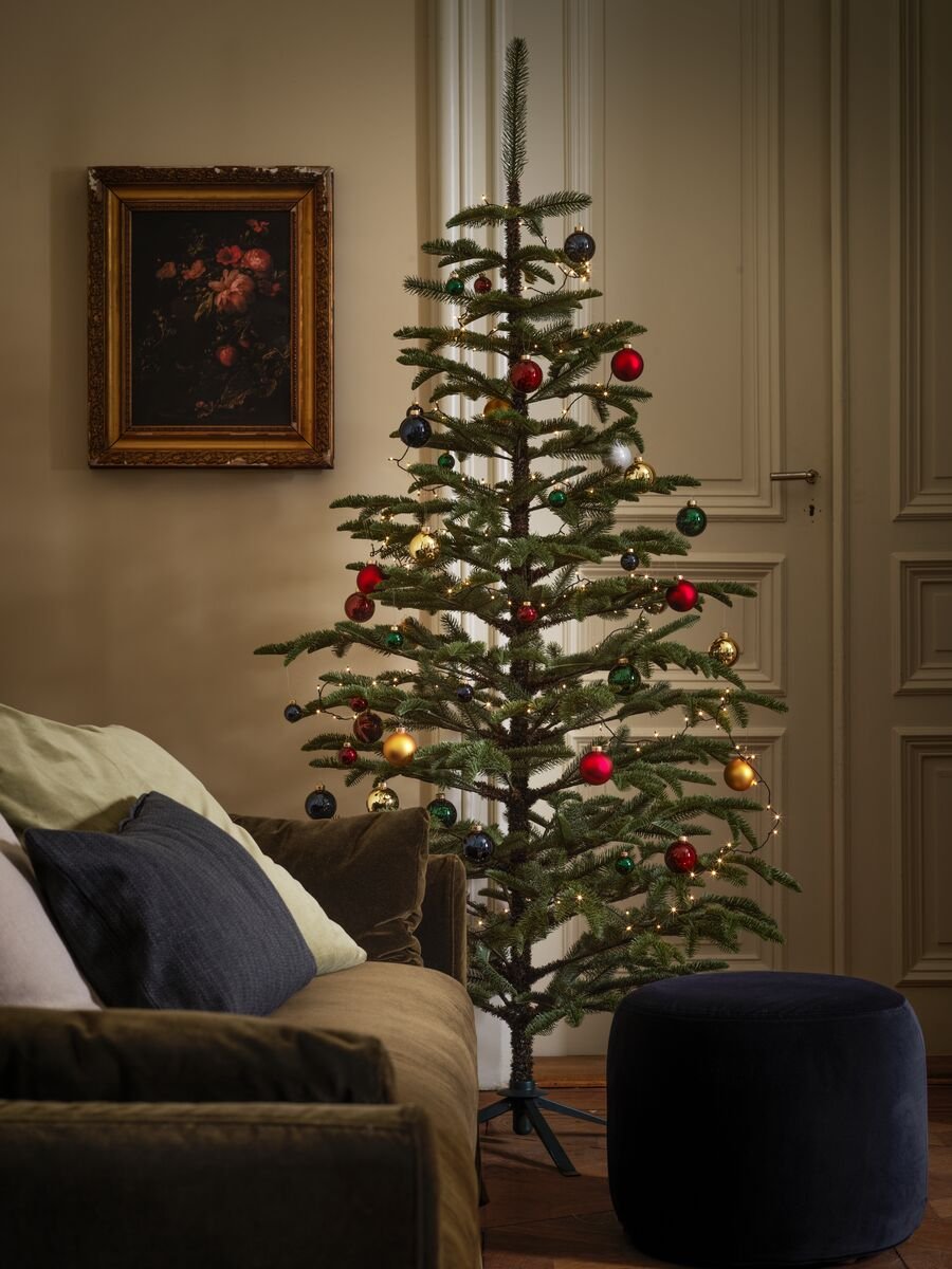 Un árbol de navidad alto frete a una ventana al costado de un sofá en una sala.