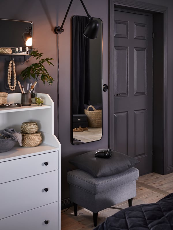 A black LINDBYN mirror, a STRANDMON footstool and HAUGA chest of drawers are in a grey-themed room.
