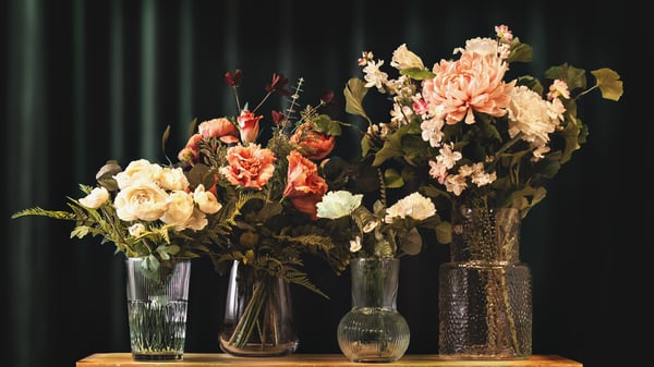 Artificial flowers and real flowers in glass vases on a dark background