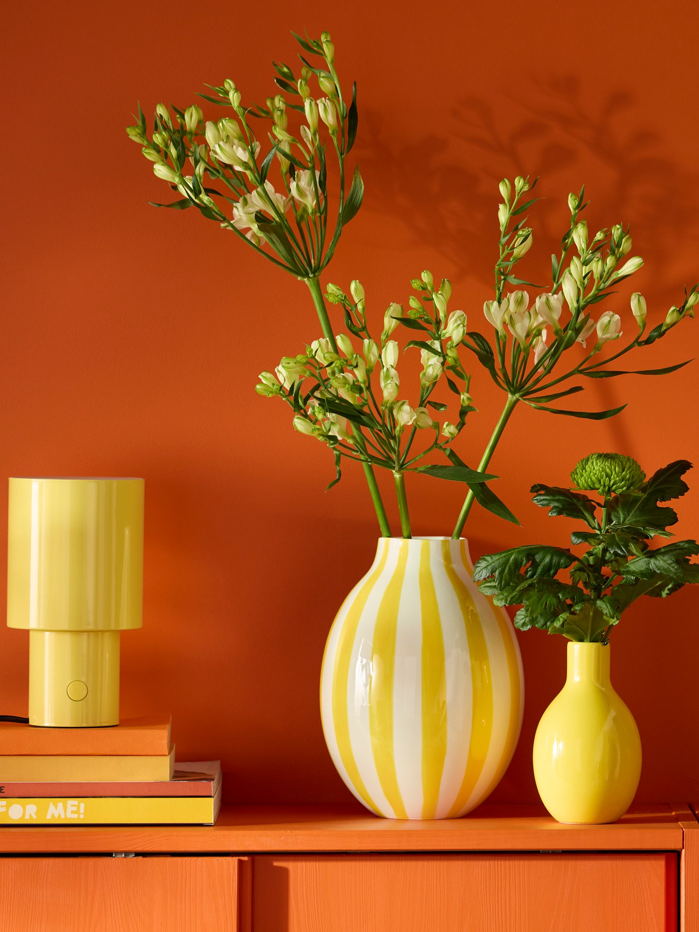 A striped white and yellow BLODBJÖRK vase sits next to a smaller yellow vase on a reddish cabinet with sliding doors.