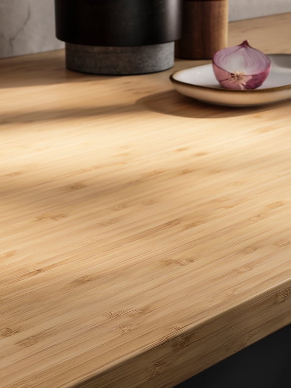 A kitchen with a HOLMARED worktop in bamboo/veneer and splashback in marble effect. There is a red onion on a GLADELIG plate.