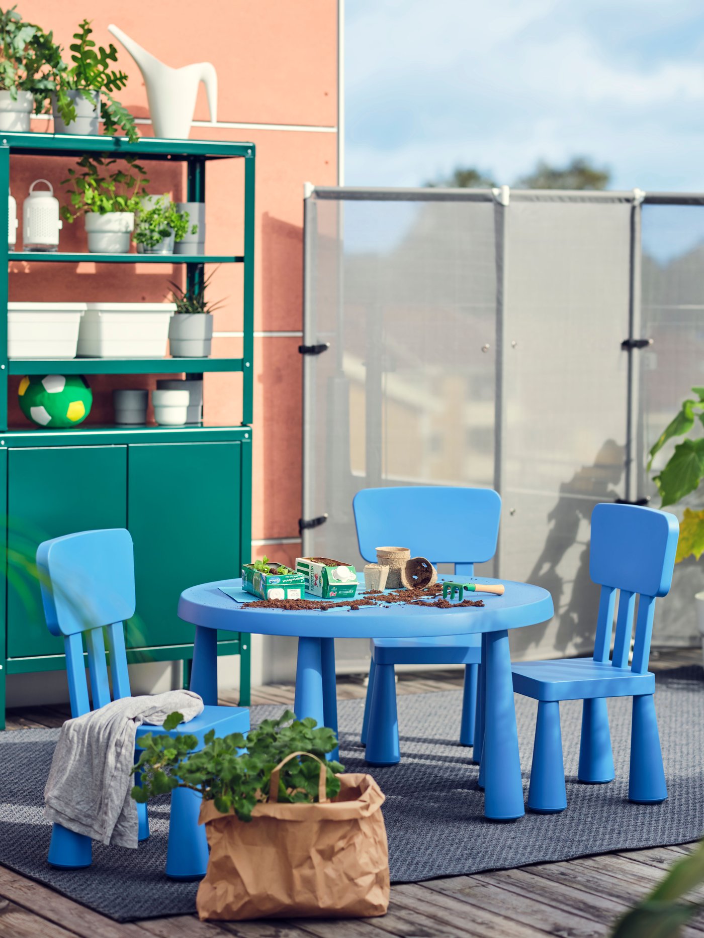 Et blåt sæt MAMMUT børnemøbler bestående af et bord og to stole står på en terrasse.