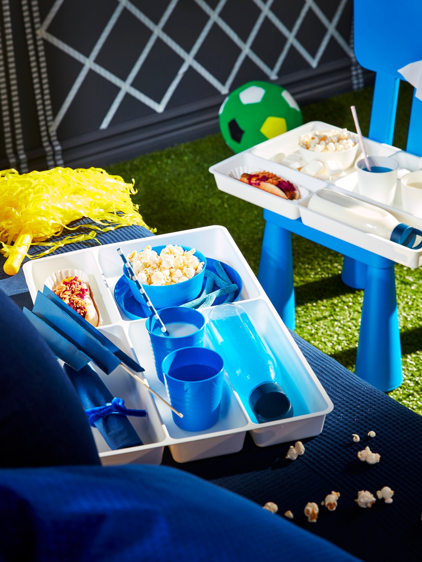 Auf einem blauen Sofa liegt ein weißes Tablett mit ÖPopcorn und Gläsern. Dasselbe steht auf einem Hocker vor dem SOfa und auf der Couch liegen Popcorn Stücke.