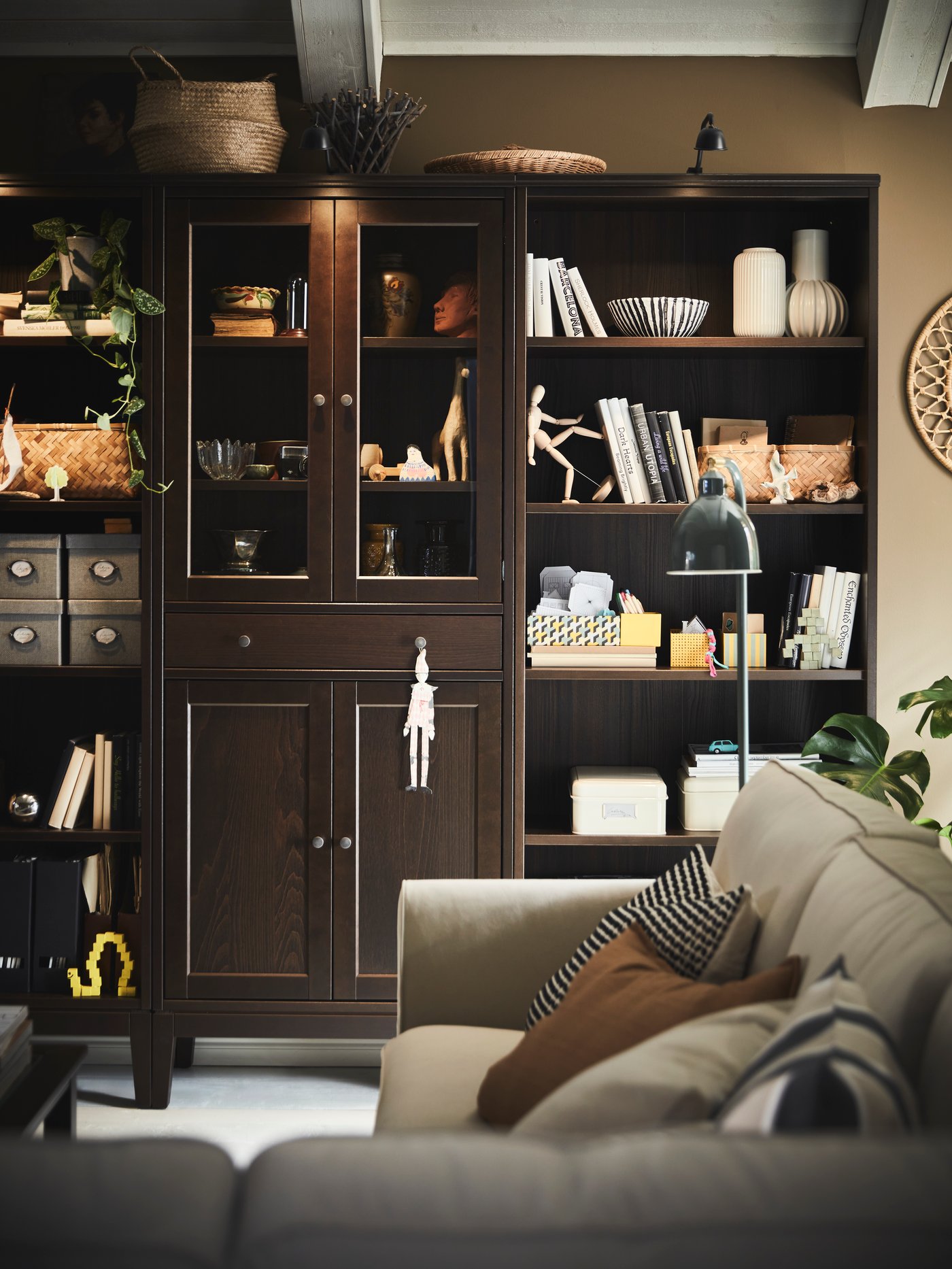 A black IDANÄS high cabinet with glass-doors and 1 drawer stands between two IDANÄS bookcases near an EKHOLMA corner sofa.