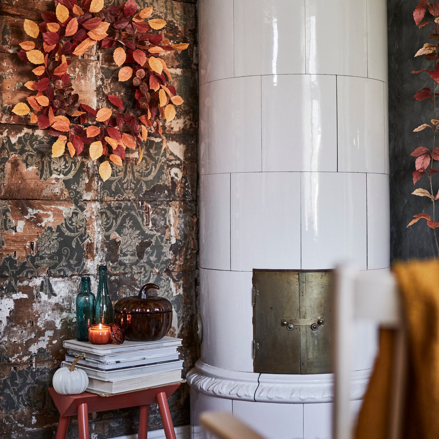 A HÖSTAGILLE artificial wreath in mixed colours adorns a rustic wall, set amidst decorative items, some books and a candle.