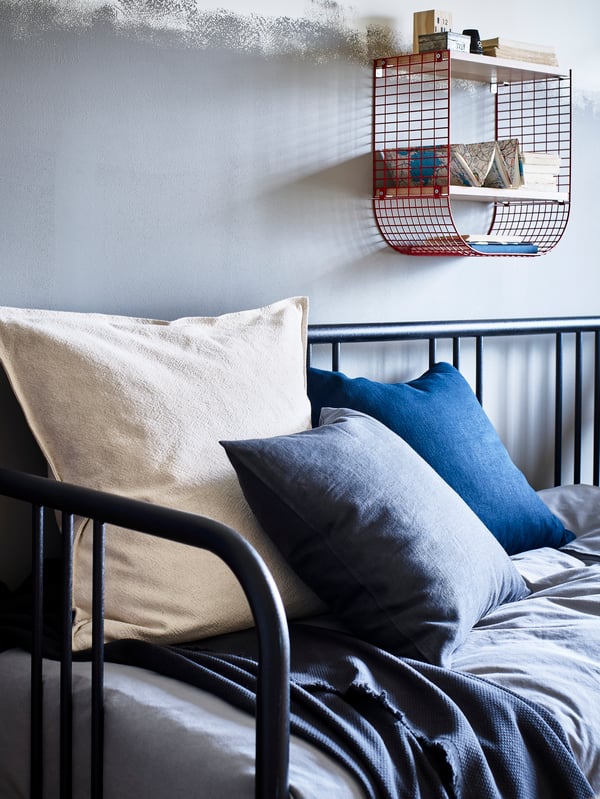 A cosy white double bed is made up in a grey GRÖNLID sofa-bed, with a wicker LUBBAN trolley beside it.
