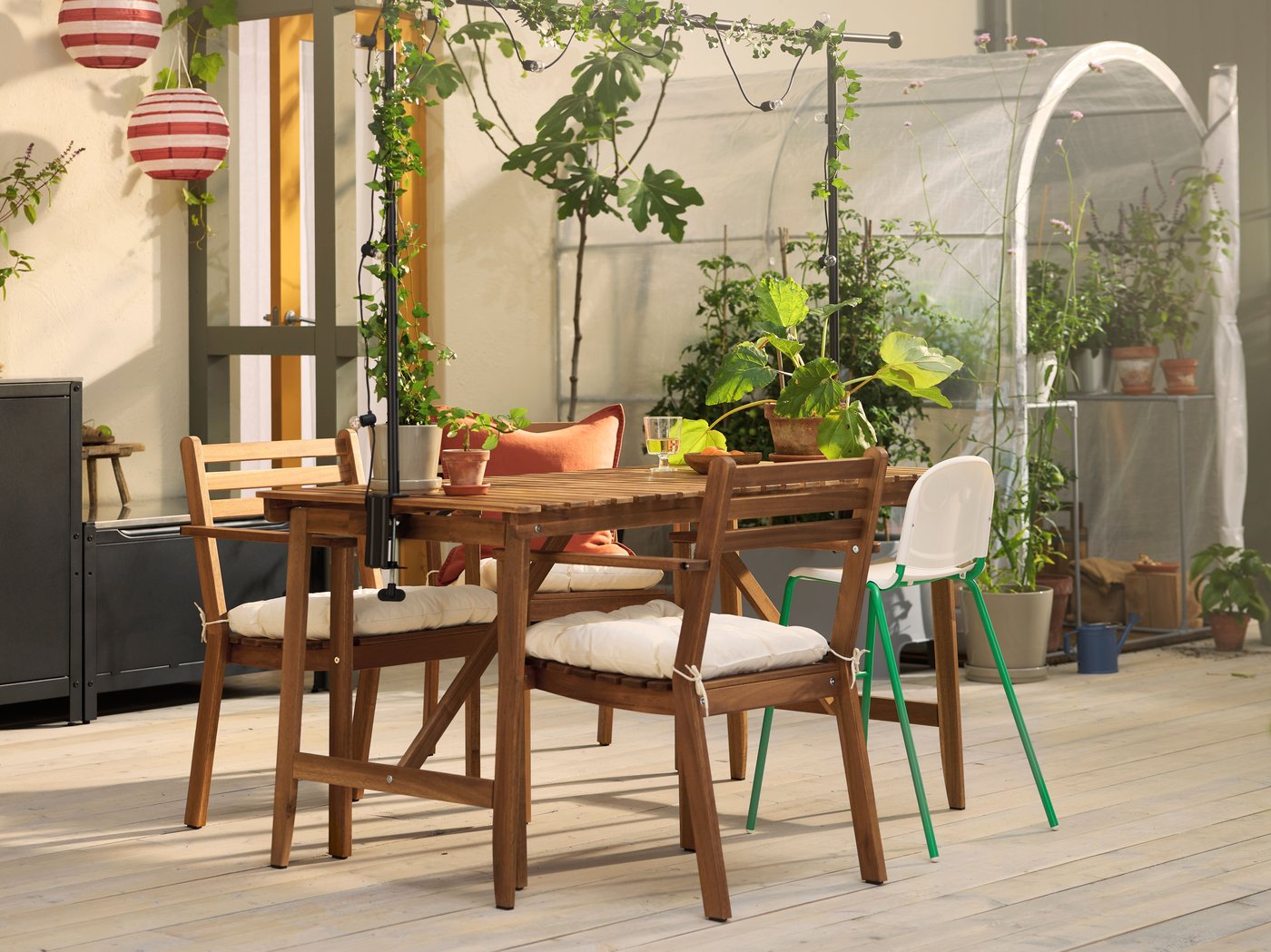 A patio with a dark brown ASKHOLMEN outdoor table and dark brown ASKHOLMEN chairs with armrests with KUDDARNA chair cushions.