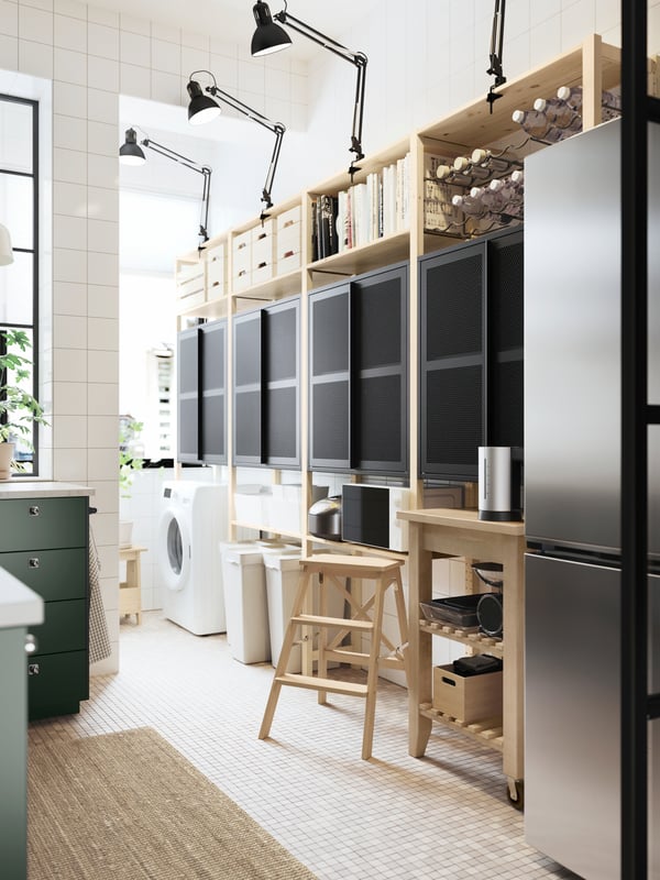 A pine IVAR shelving unit with two black mesh cabinets with doors and dark grey work lamps up top, plus a kitchen trolley.