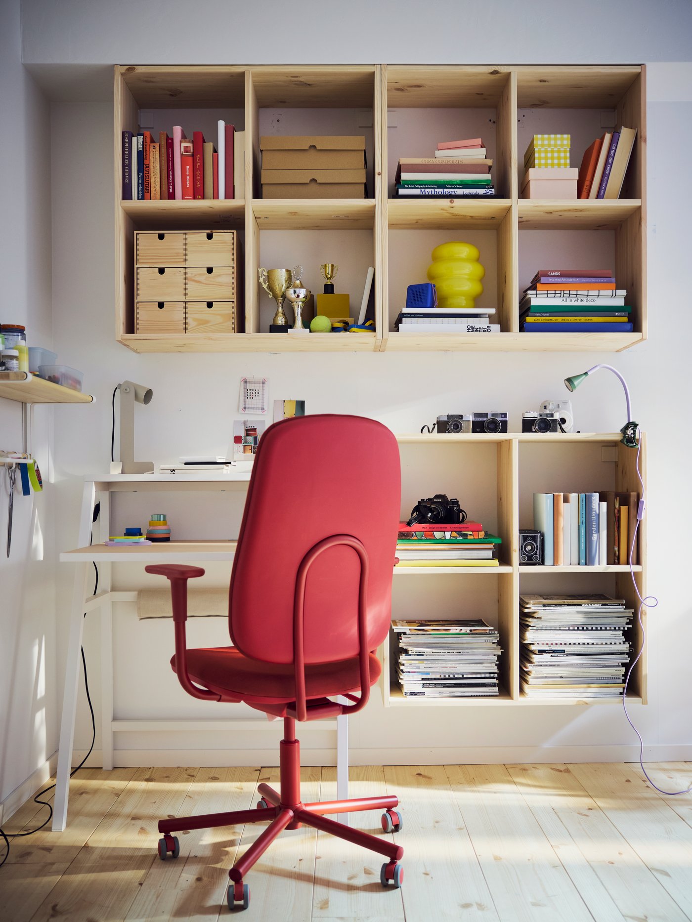 The back of a red SMÖRKULL office chair in front of a desk surrounded by IVAR shelving units in pine.