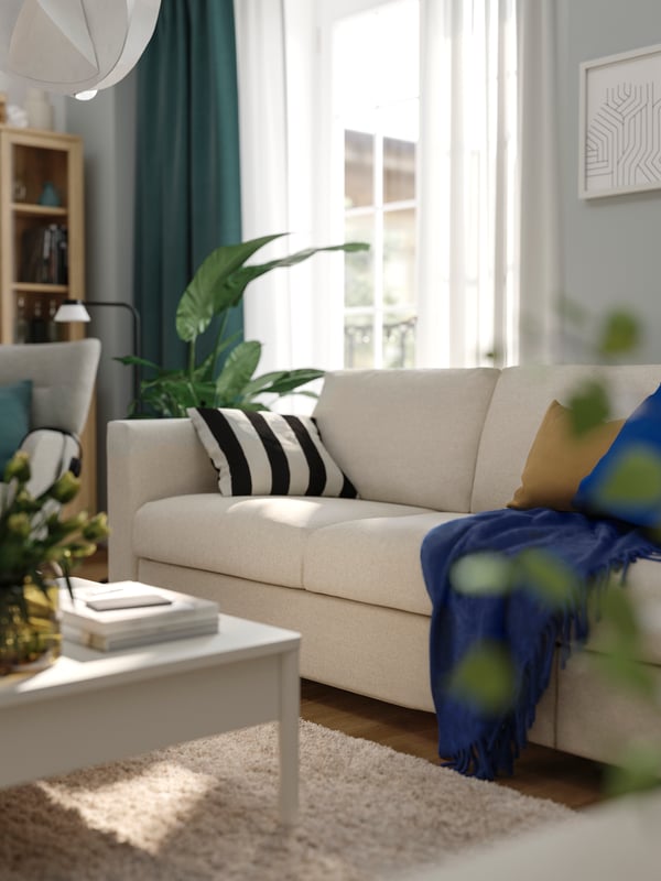 A beige FINNALA sofa in a light-filled living room with colourful cushions, TONSTAD coffe table and KLIPPOXEL blue throw.