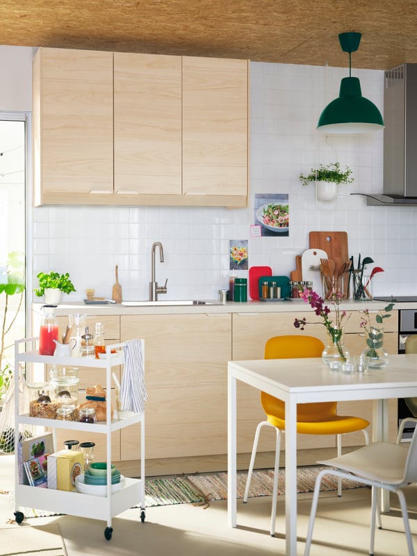 A kitchen with SEKTION cabinets, a white MELLTORP table, different-color LEIFARNE chairs, and a white NISSAFORS trolley.