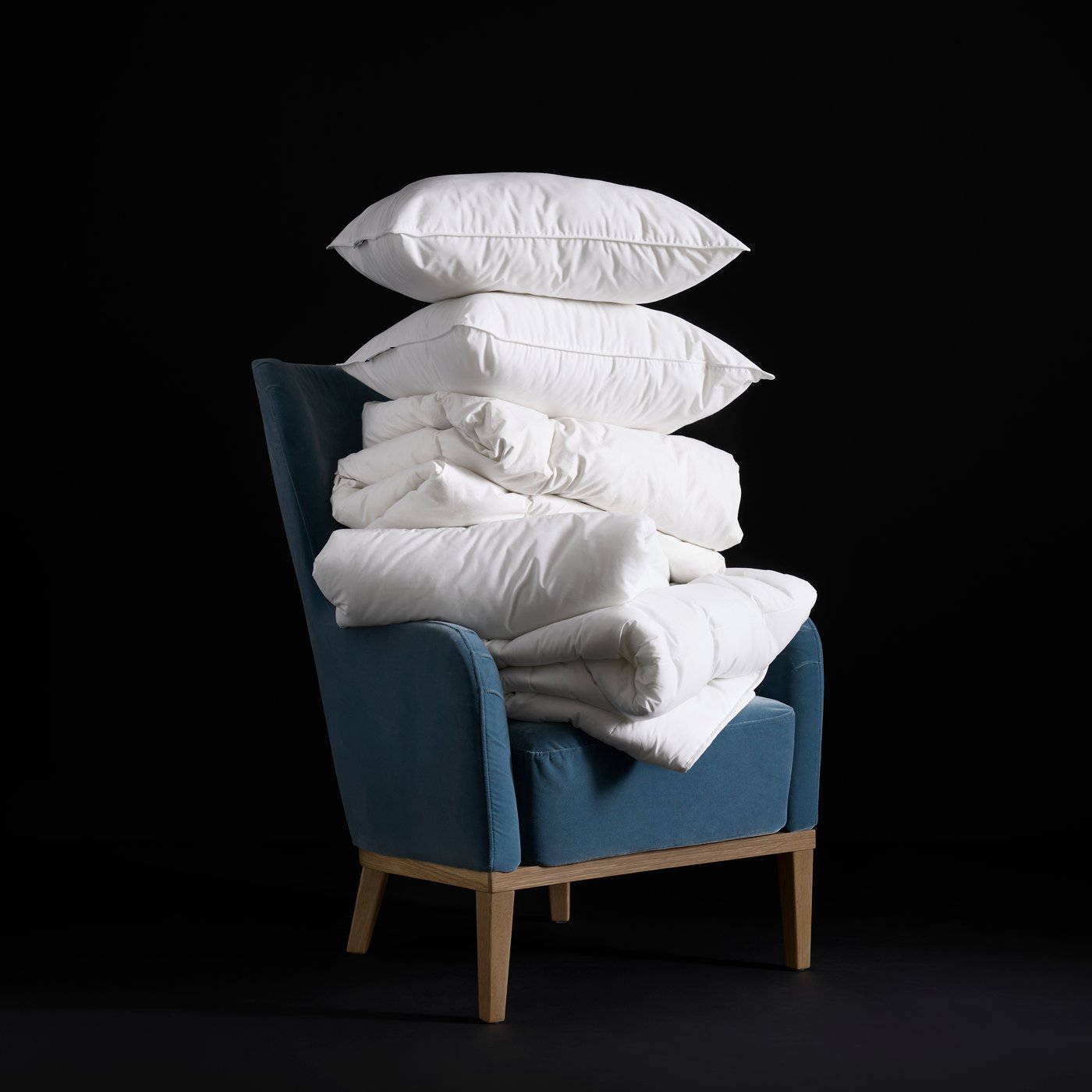 Un sillón con almohadas blancas apiladas y un duvet blanco doblado, ambos sin fundas.