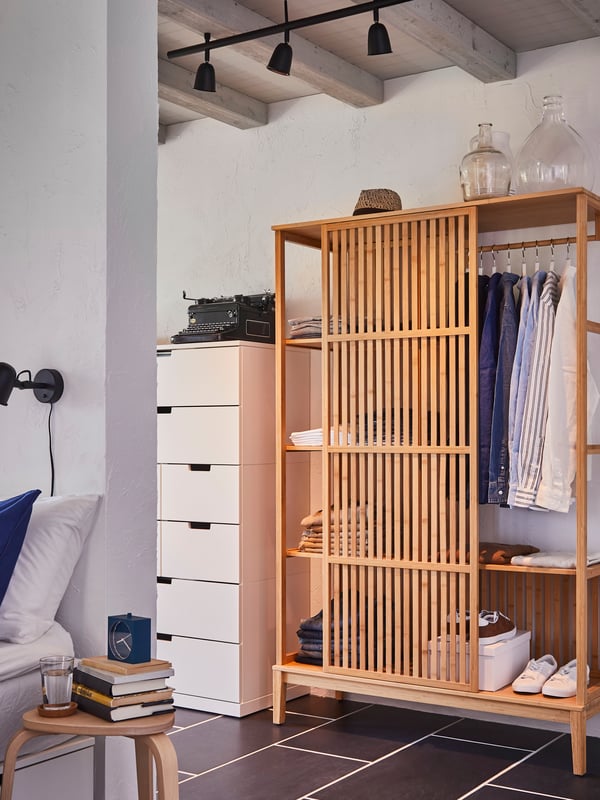 Bamboo wooden minimalistic NORDKISA wardrobe with sliding front doors showing organisation of clothes with BUMERANG hangers in the bedroom next to a chest of drawers. 