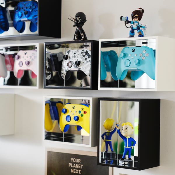 Six YXSTABY gaming controller display boxes hang on a white wall, displaying different colours controllers and collectibles.