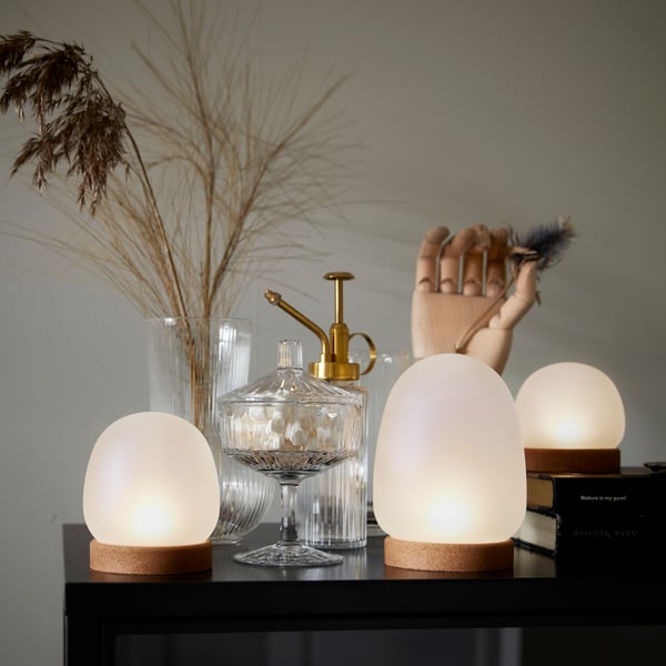A close-up of a BONDHOLMEN outdoor table with some plates, glasses and a black STORHAGA LED table lamp on it.
