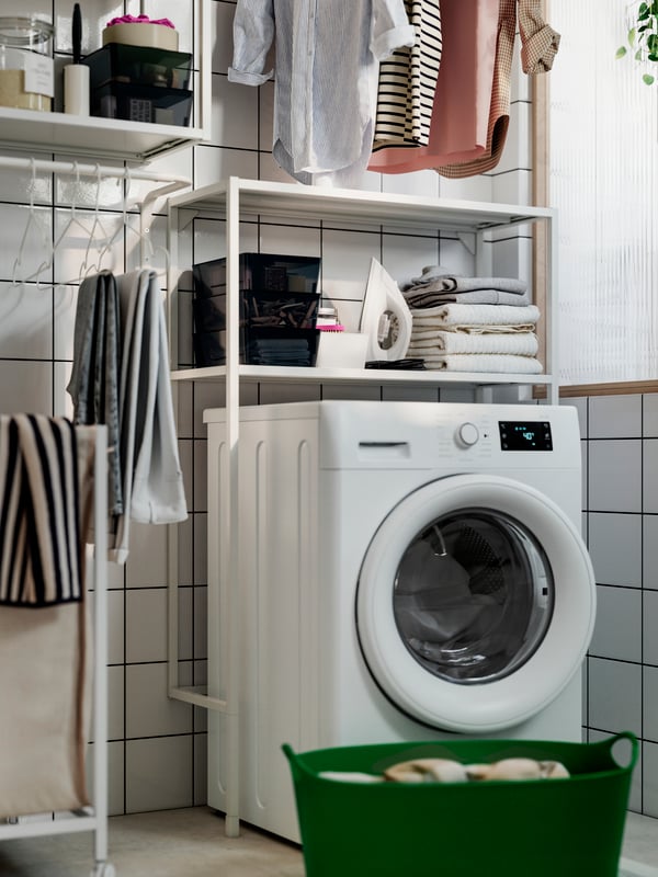Donkergroene TORKIS wasmand staat op de grond in de badkamer, vóór een witte wasmachine en ENHET bovenkastelementen.