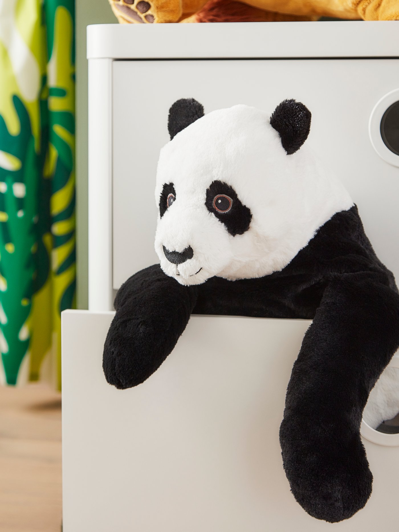 Un oso panda de peluche asomándose desde un cajón de una cómoda blanca.