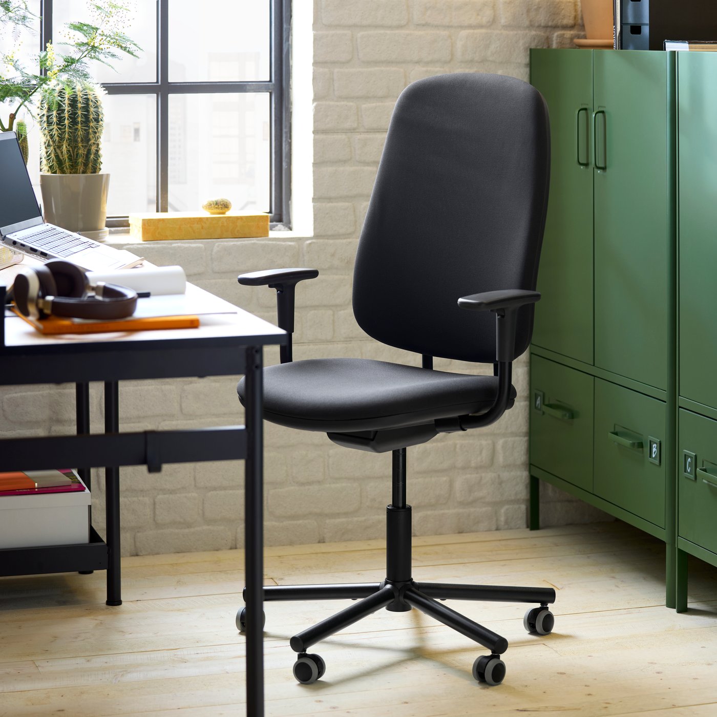 A dark green IDÅSEN cabinet with closed doors and two drawers stands behind a dark grey SMÖRKULL office chair.