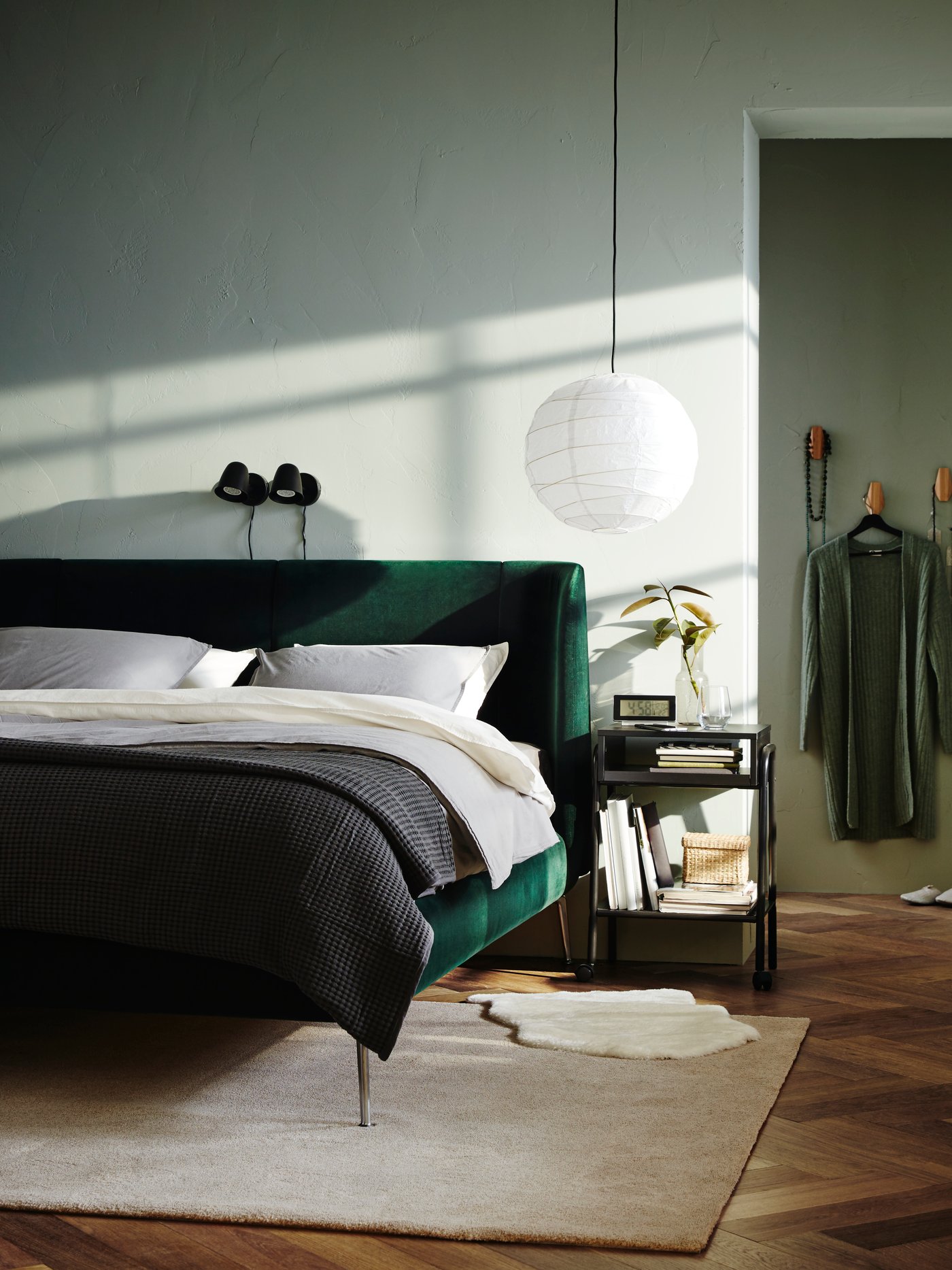 Una habitación matrimonial con una cama TUFJORD con tapiz verde y ropa de cama blanca. Al costado de la cama una mesita de noche con una lámpara de mesa.