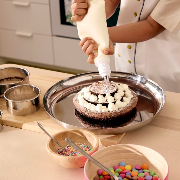 A chocolate cake in three layers, being decorated with little dots of cream with the help of SMAKSAM piping tool.