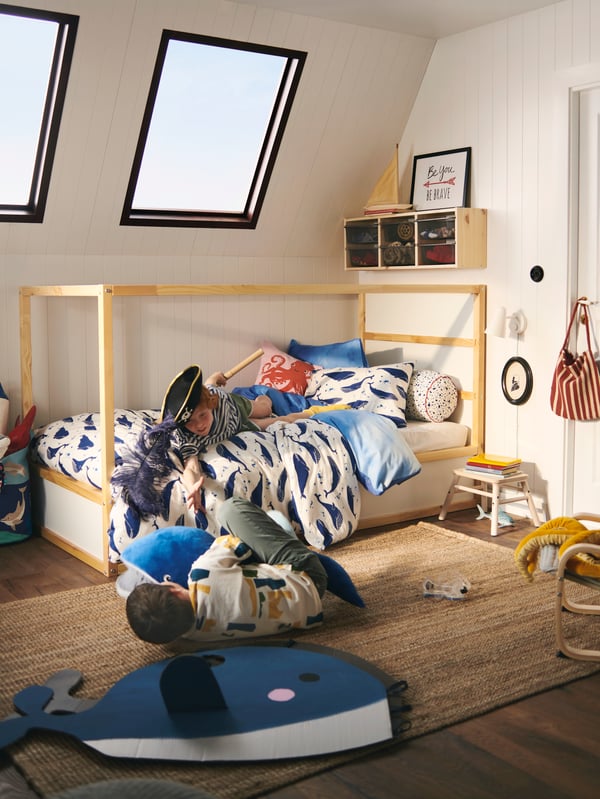 A boy plays on a bed dressed in a BLÅVINGAD blue whale duvet cover with another boy, playing with a BLÅVINGAD whale toy.